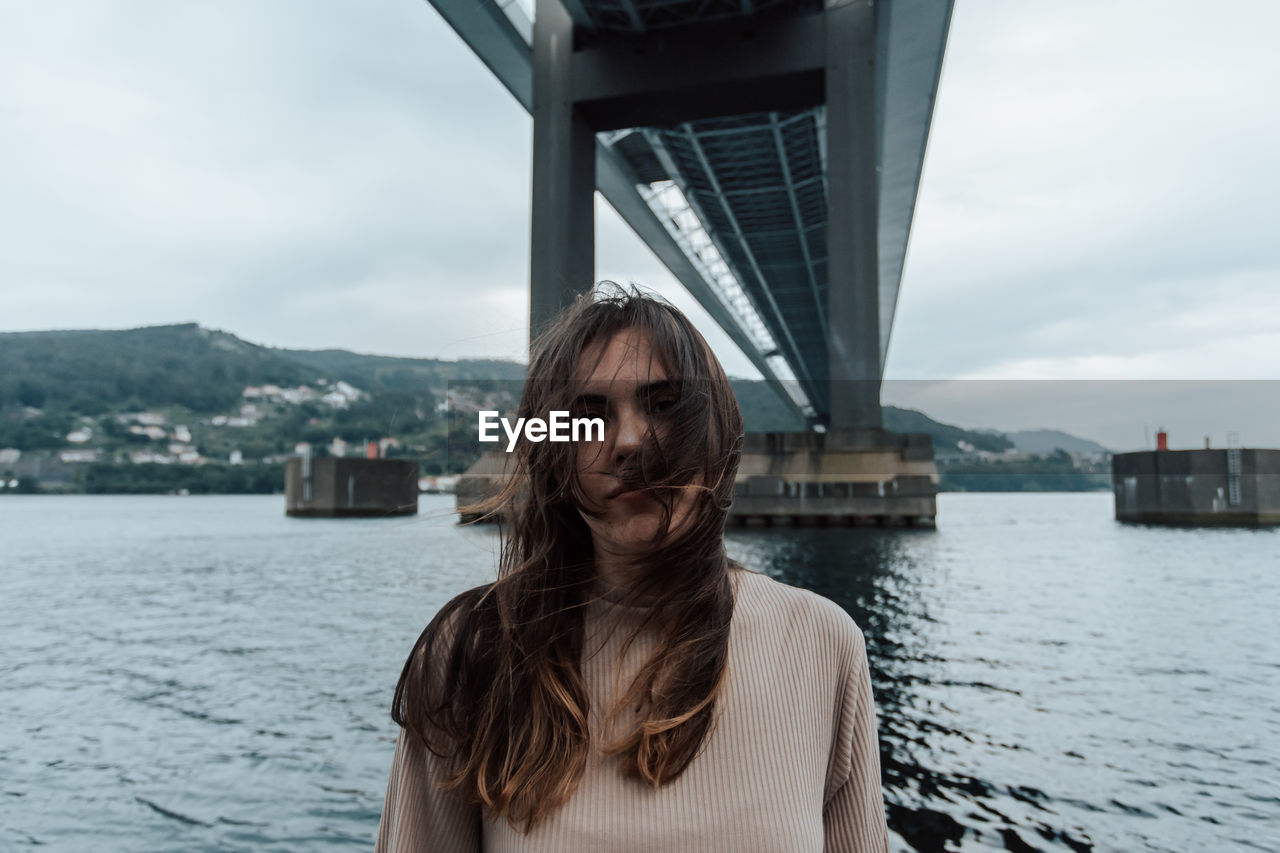 portrait of young woman standing against river in city