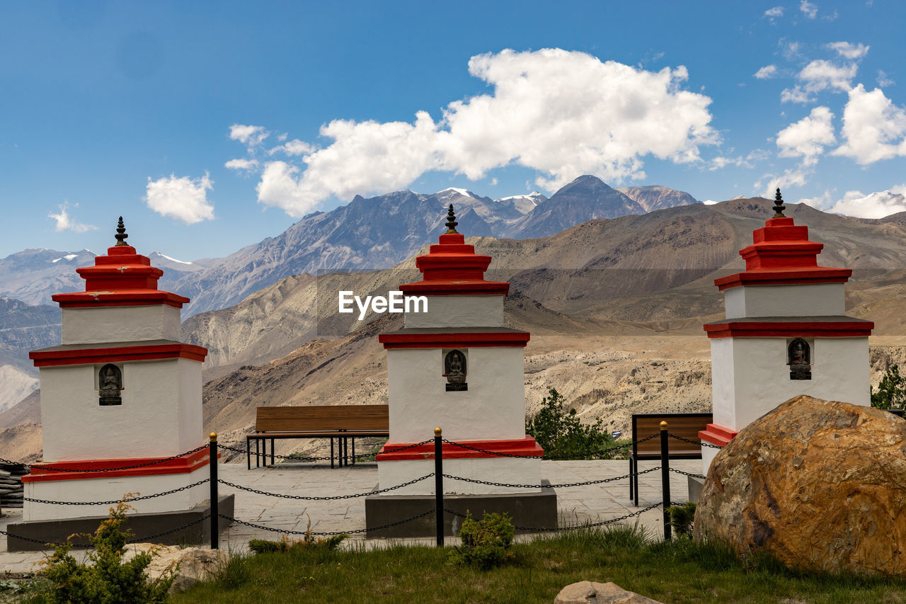 architecture, mountain, travel destinations, religion, travel, built structure, building, sky, building exterior, belief, landscape, history, cloud, nature, temple - building, the past, environment, tourism, scenics - nature, ancient, spirituality, place of worship, tower, mountain range, tradition, beauty in nature, red, no people, outdoors, land, vacation, landmark, pagoda, temple, city, flag, plant, holiday, tranquility, shrine, blue, snow, trip, day, palace, tranquil scene