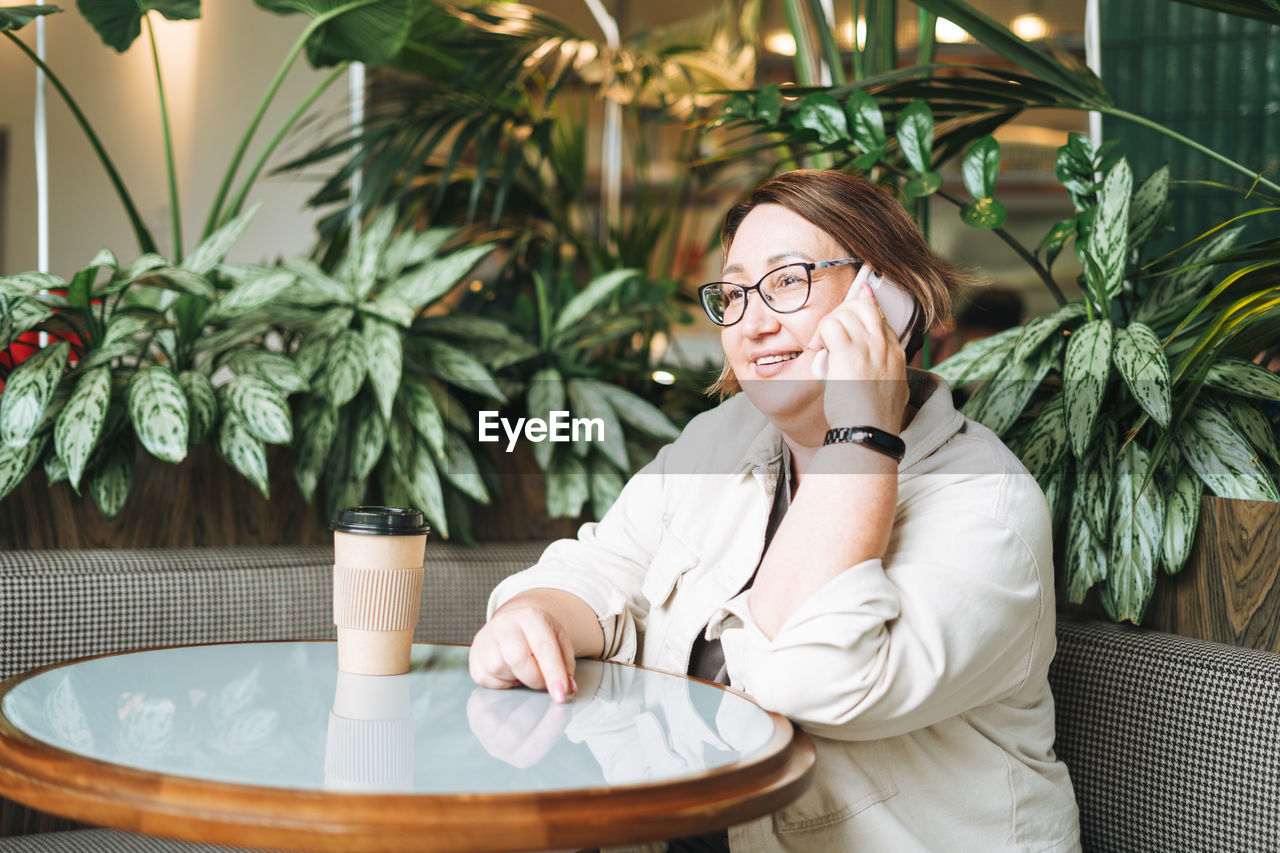 Adult middle aged woman plus size in casual clothes with coffee using mobile phone in cafe