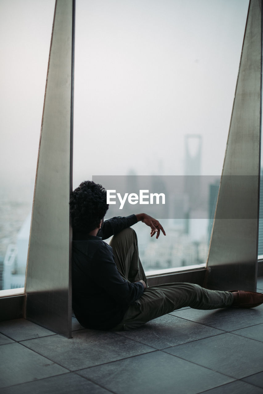 Full length of man sitting by window in building