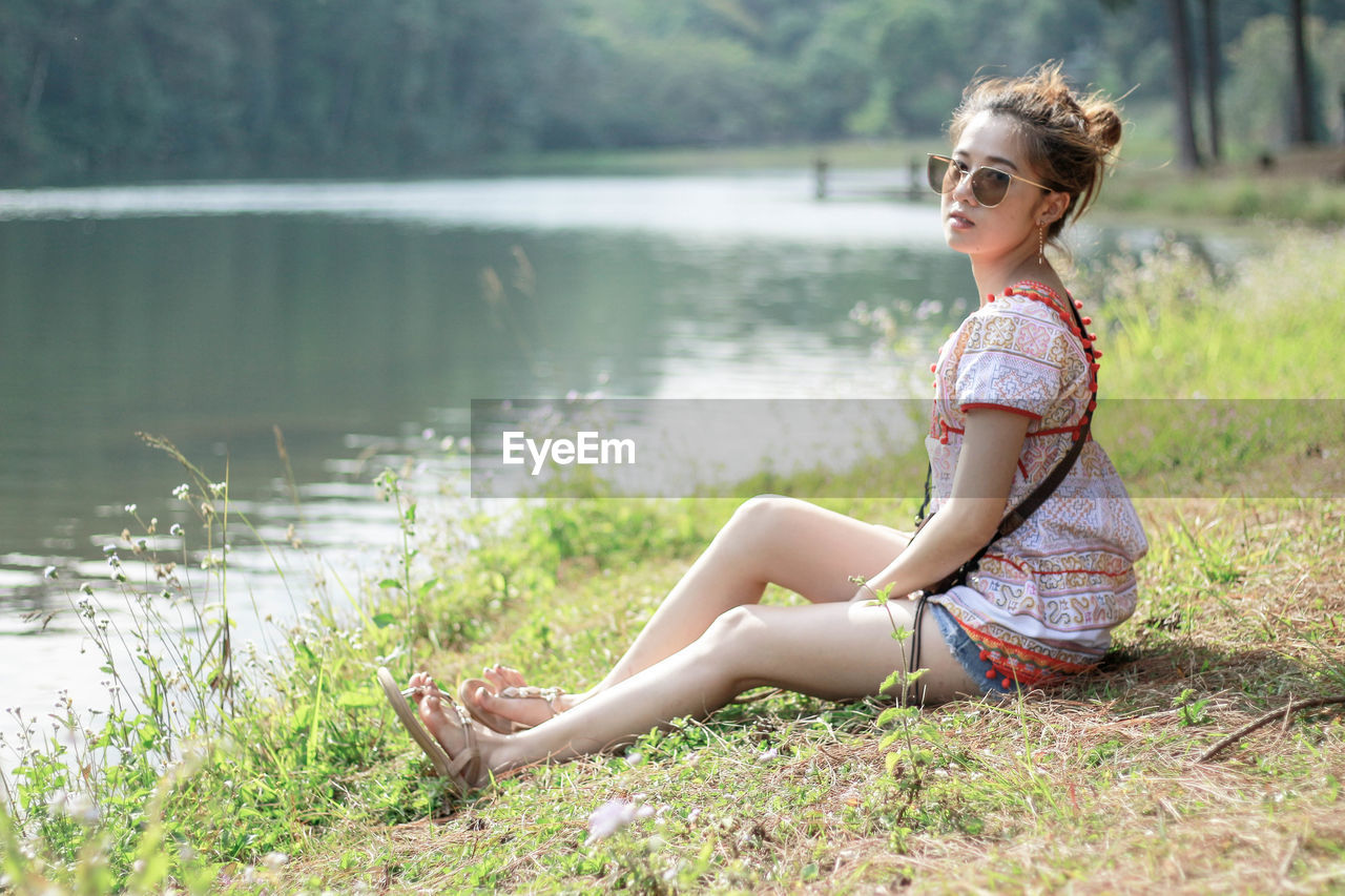 Portrait of woman sitting on grass by lake