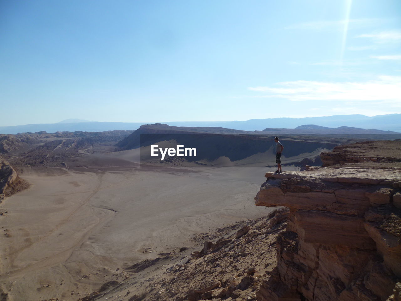 Mid distance view of man standing on cliff at desert during sunny day