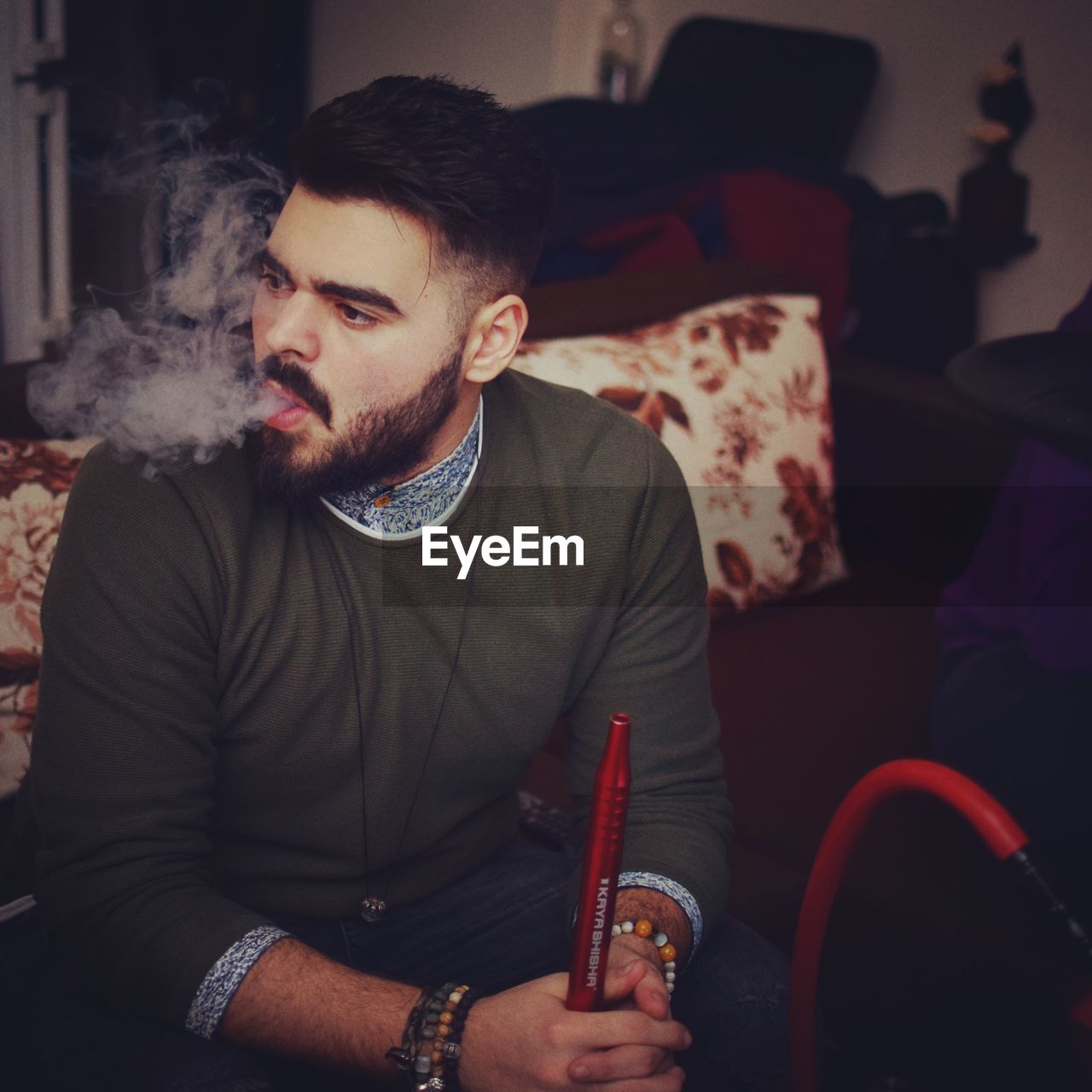 Young man smoking hookah while sitting at home