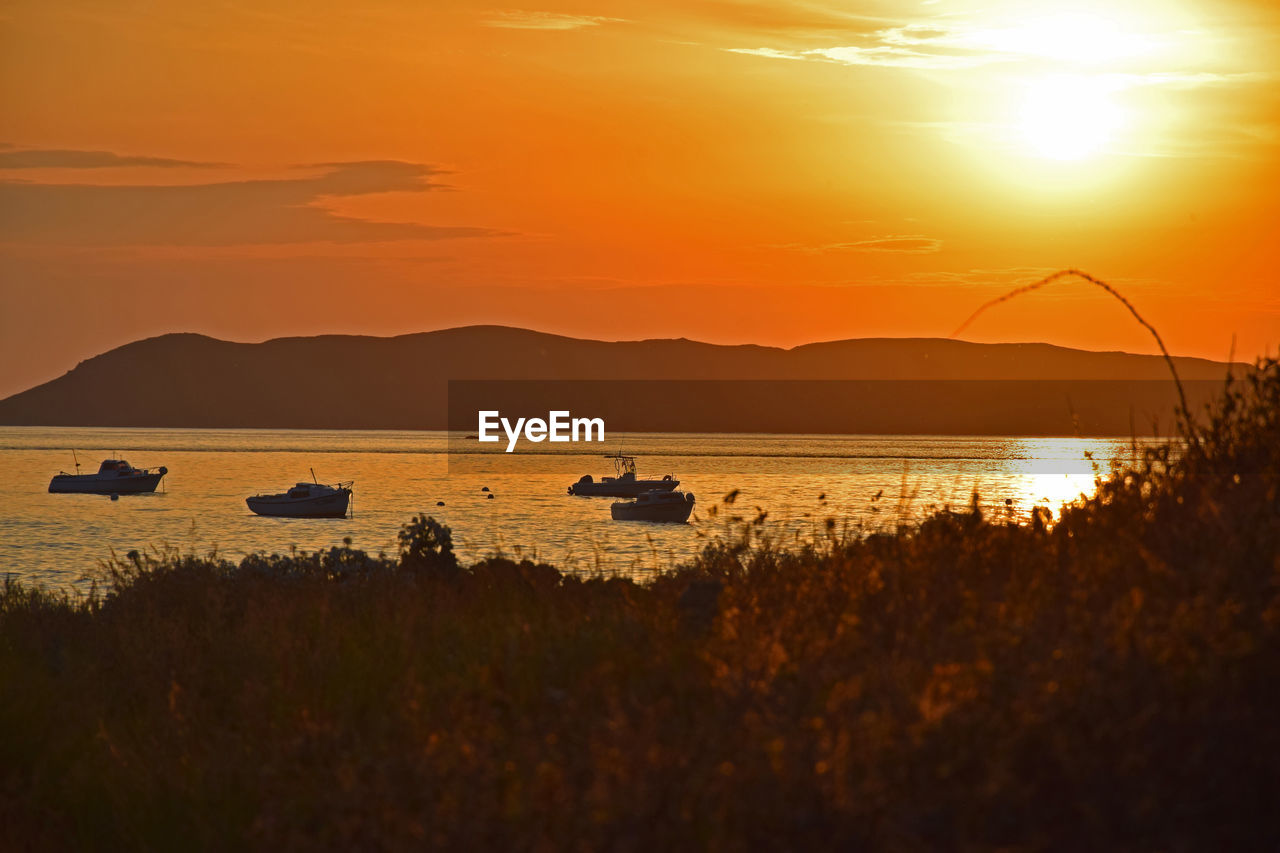 SILHOUETTE BOATS ON LAKE AGAINST ORANGE SKY