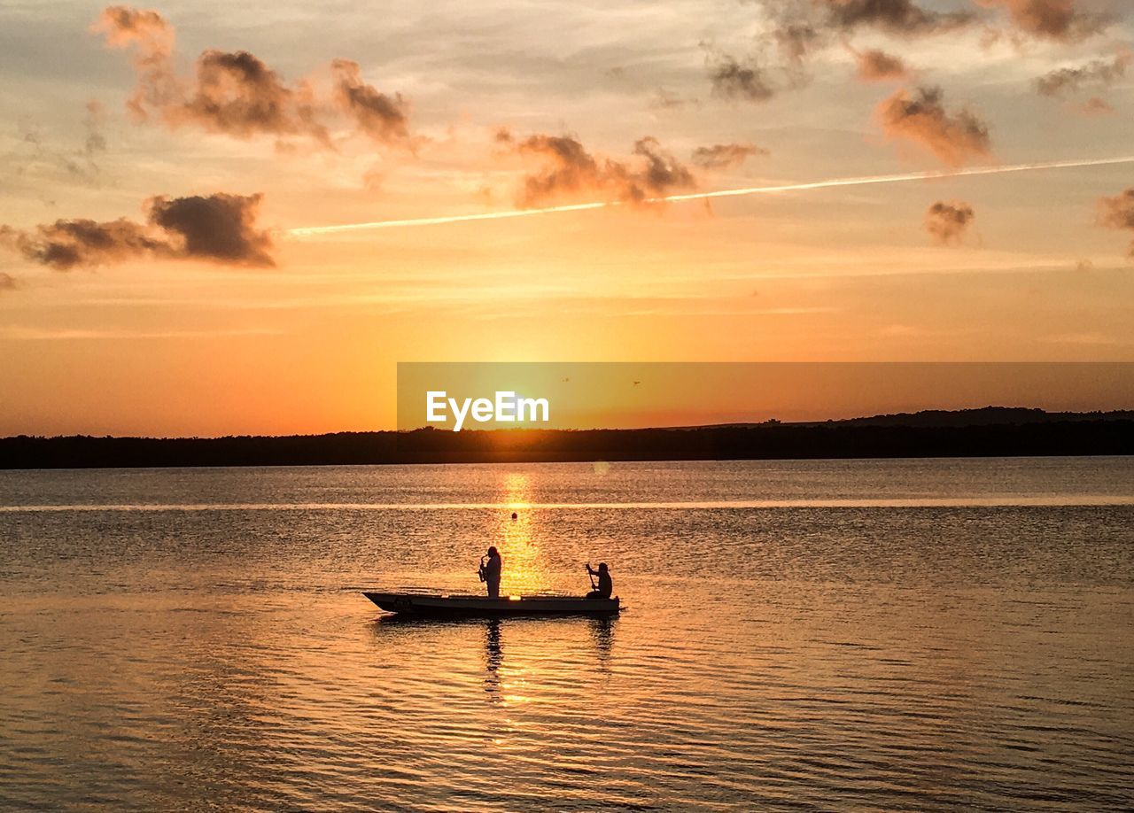 Silhouette men in boat on sea against sky during sunset