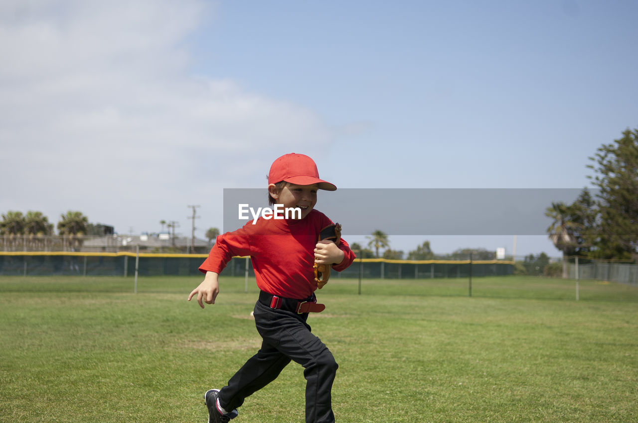 Young boy holding his glove and running across the tball field