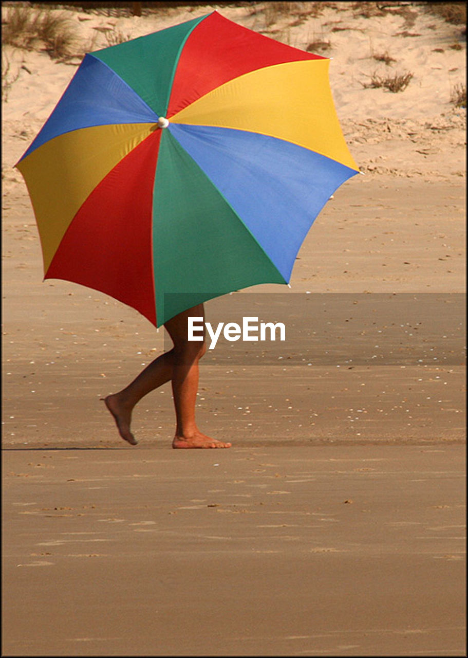 LOW SECTION OF WOMAN WALKING AT BEACH