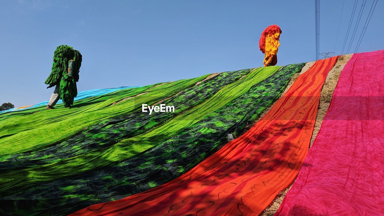 Low angle view of people carrying textile while walking on mountain against sky