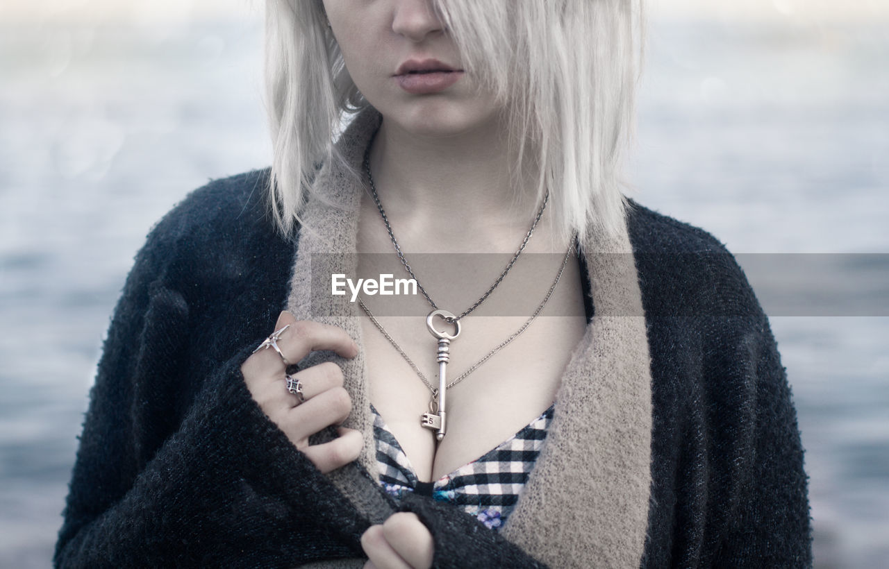 Midsection of beautiful young woman wearing chain with key pendant at beach