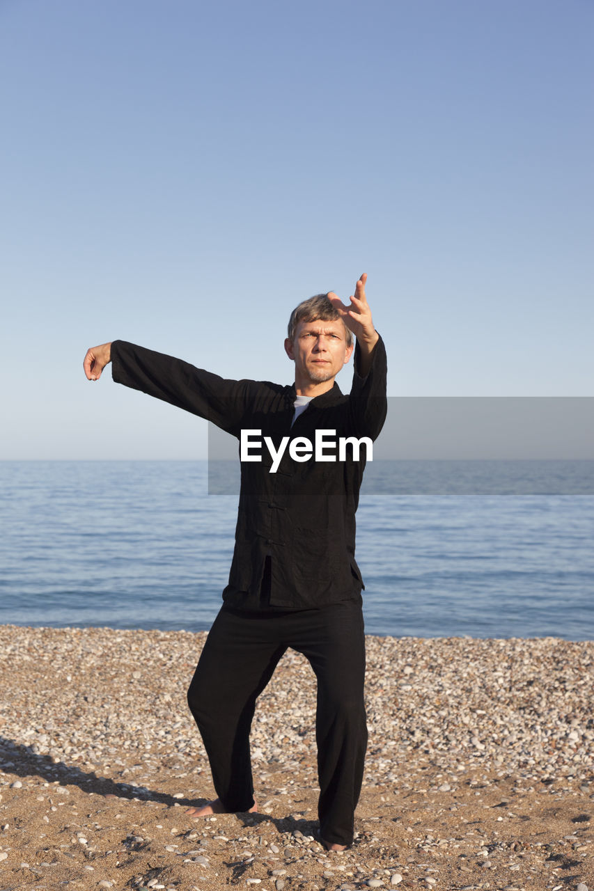 Full length of man exercising at beach against clear sky