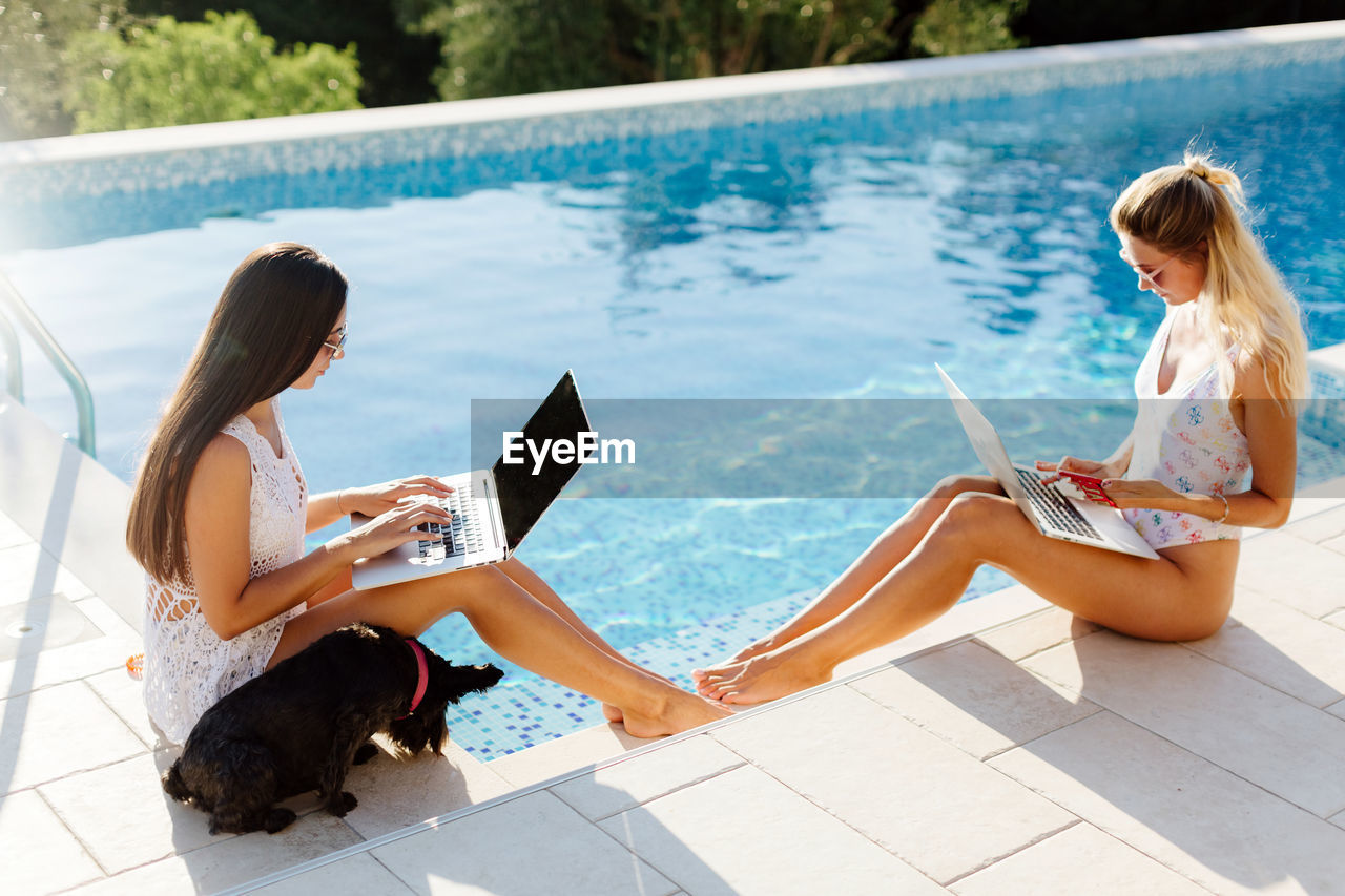 High angle view of women using laptop while sitting by swimming pool
