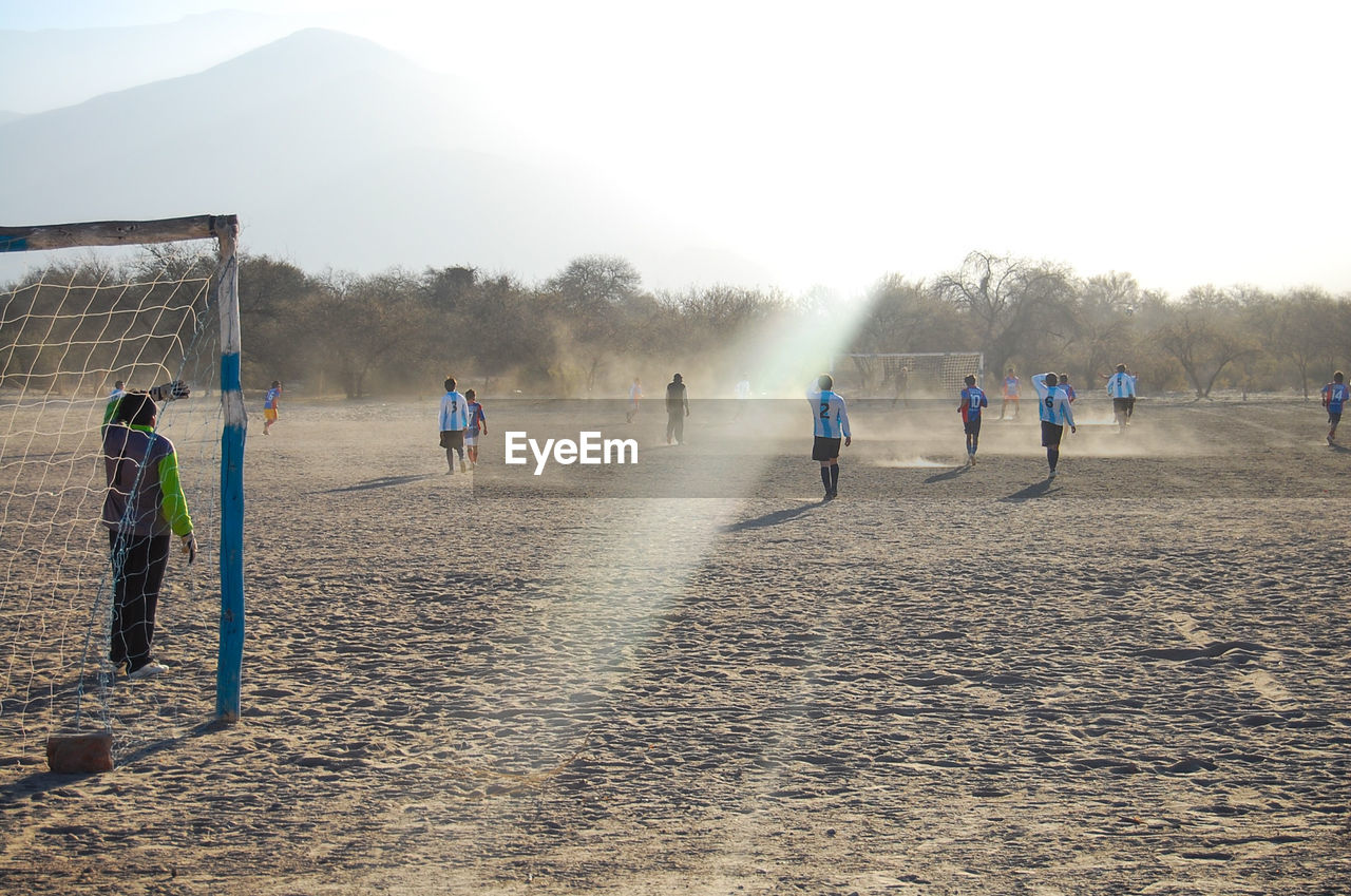 People playing soccer on field during sunny day