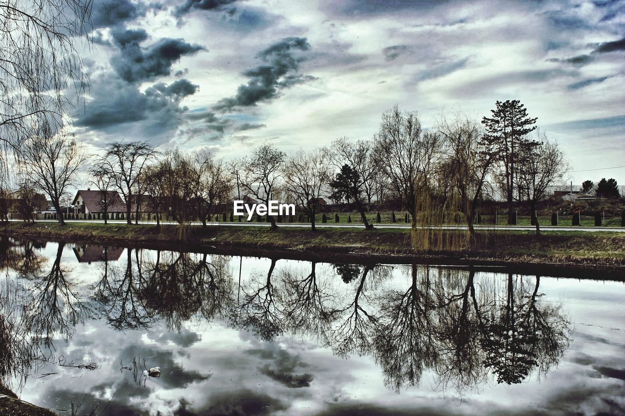 Reflection of trees in river against cloudy sky