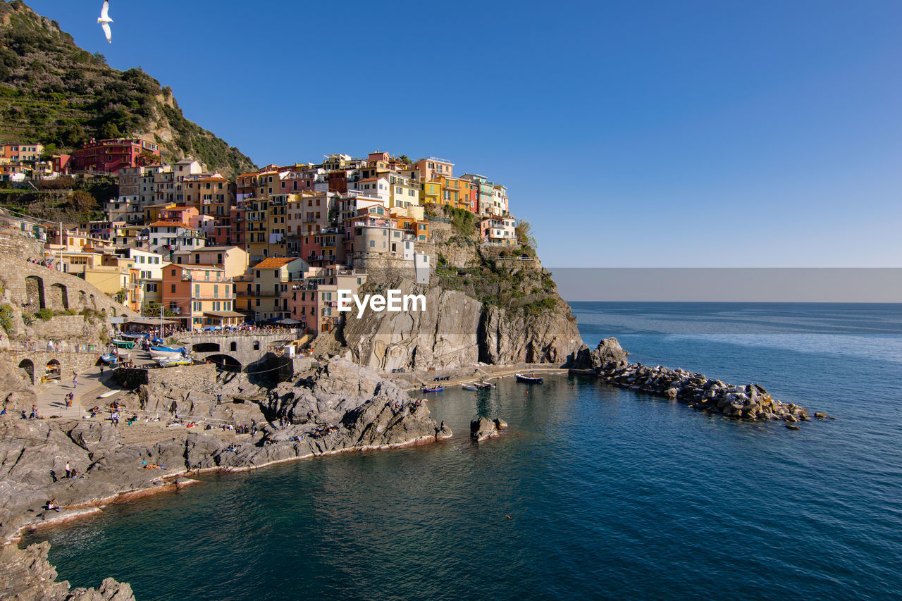 Scenic view of sea by townscape against clear blue sky