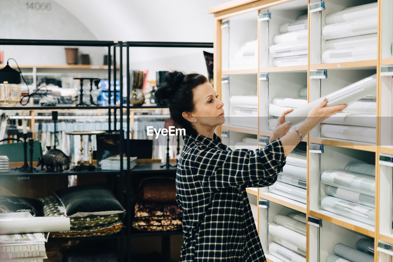 Side view of saleswoman arranging wallpaper in rack