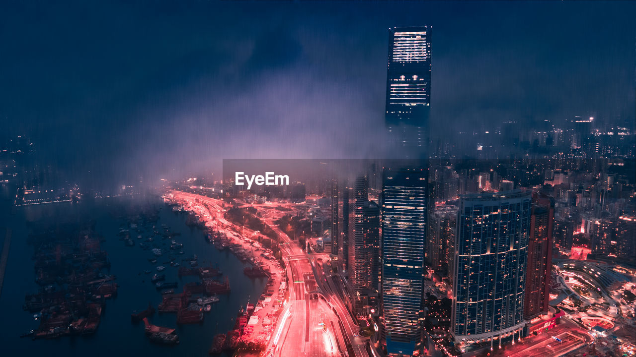 Illuminated cityscape against rainy sky at night with a cyberpunk feeling