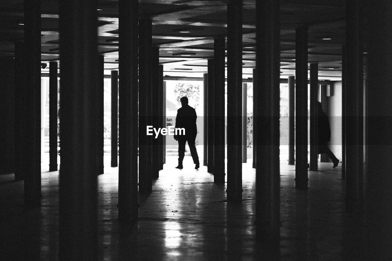 Silhouette people walking amidst columns in building