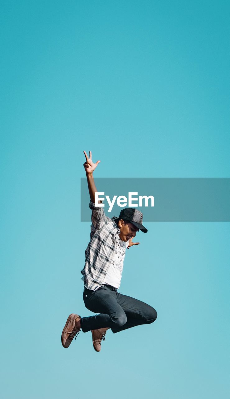 LOW ANGLE VIEW OF MAN JUMPING AGAINST BLUE SKY