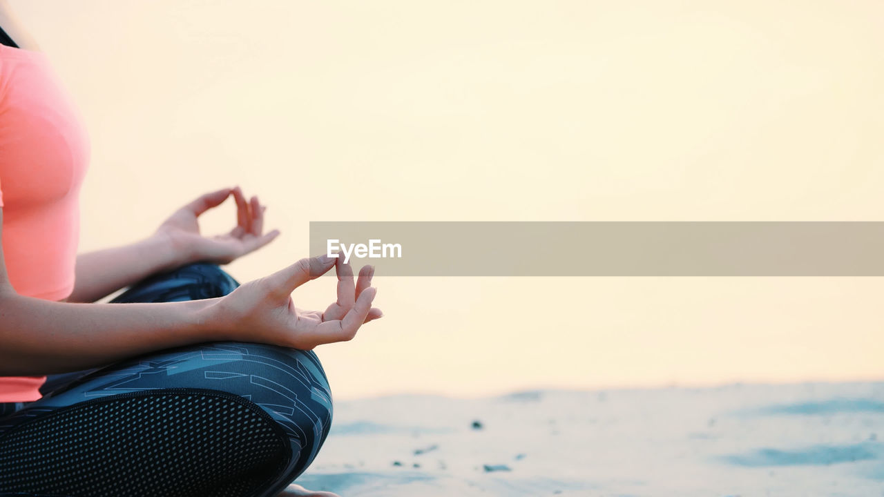 Healthy, young beautiful woman meditating, practicing yoga on the beach, by the sea, at sunrise