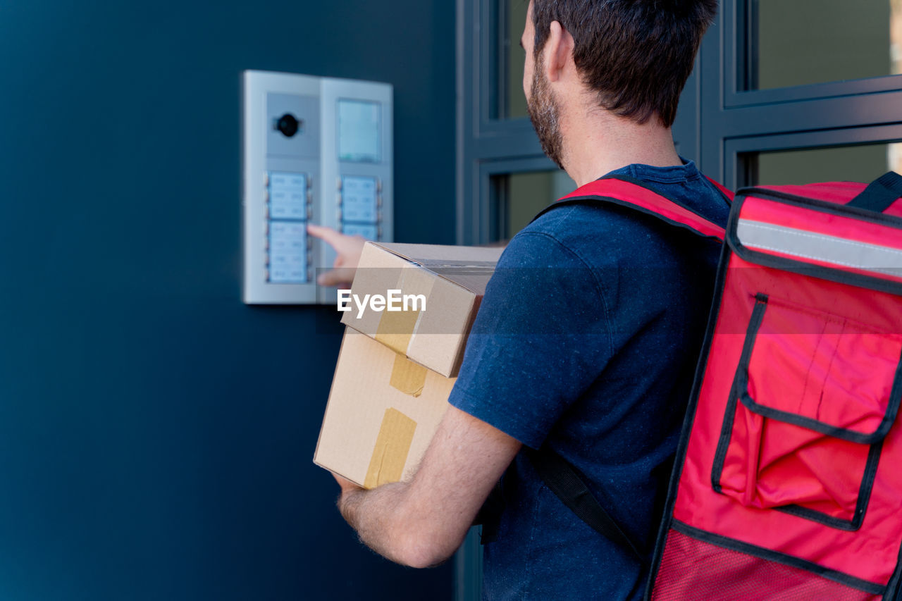 Midsection of delivery person holding parcel ringing doorbell