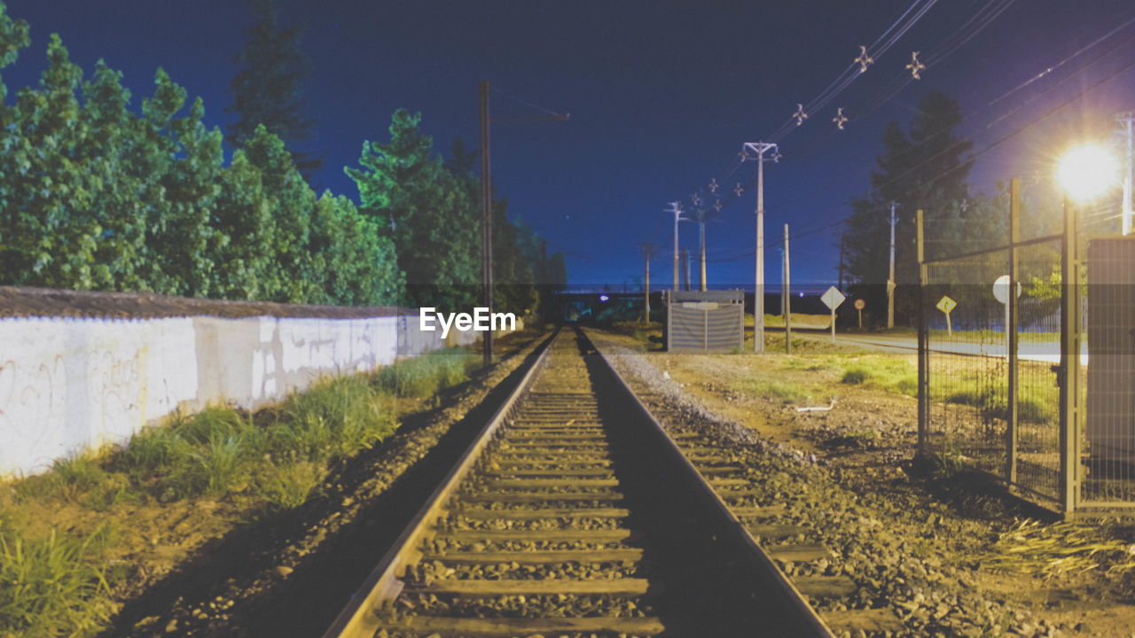 Railway tracks amidst trees against sky at night