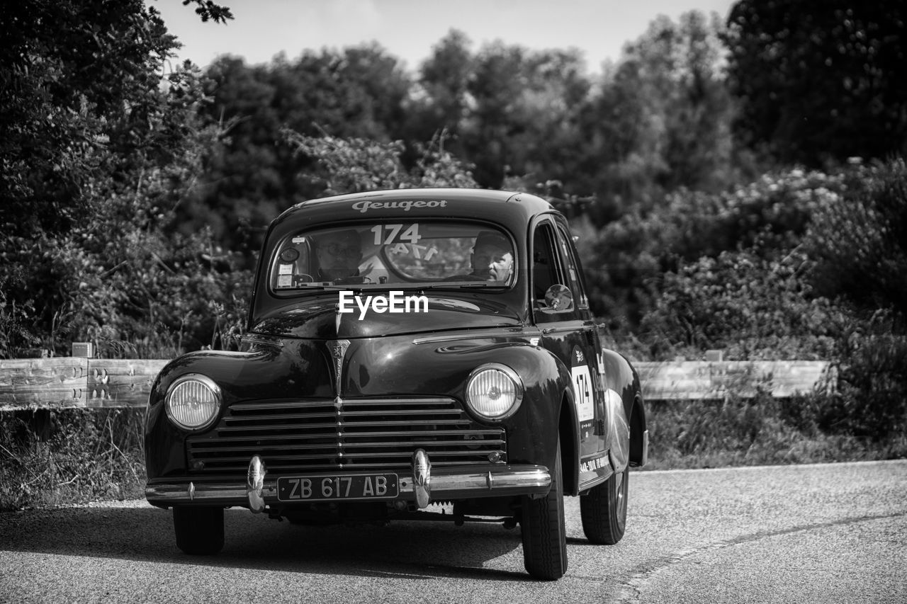 VINTAGE CAR ON ROAD BY TREES