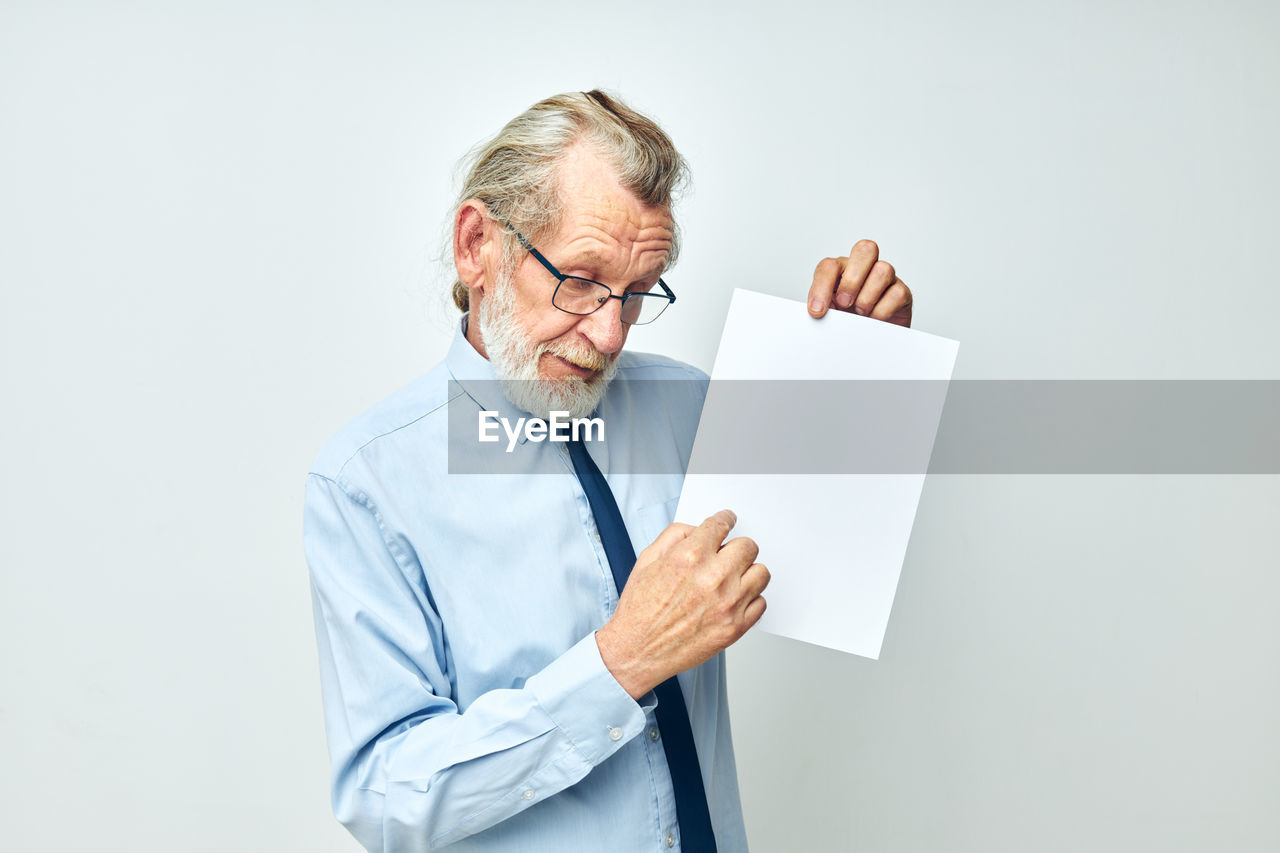 portrait of senior man holding paper while standing against white background