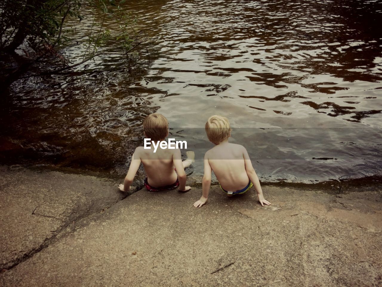 Rear view of children sitting near lake