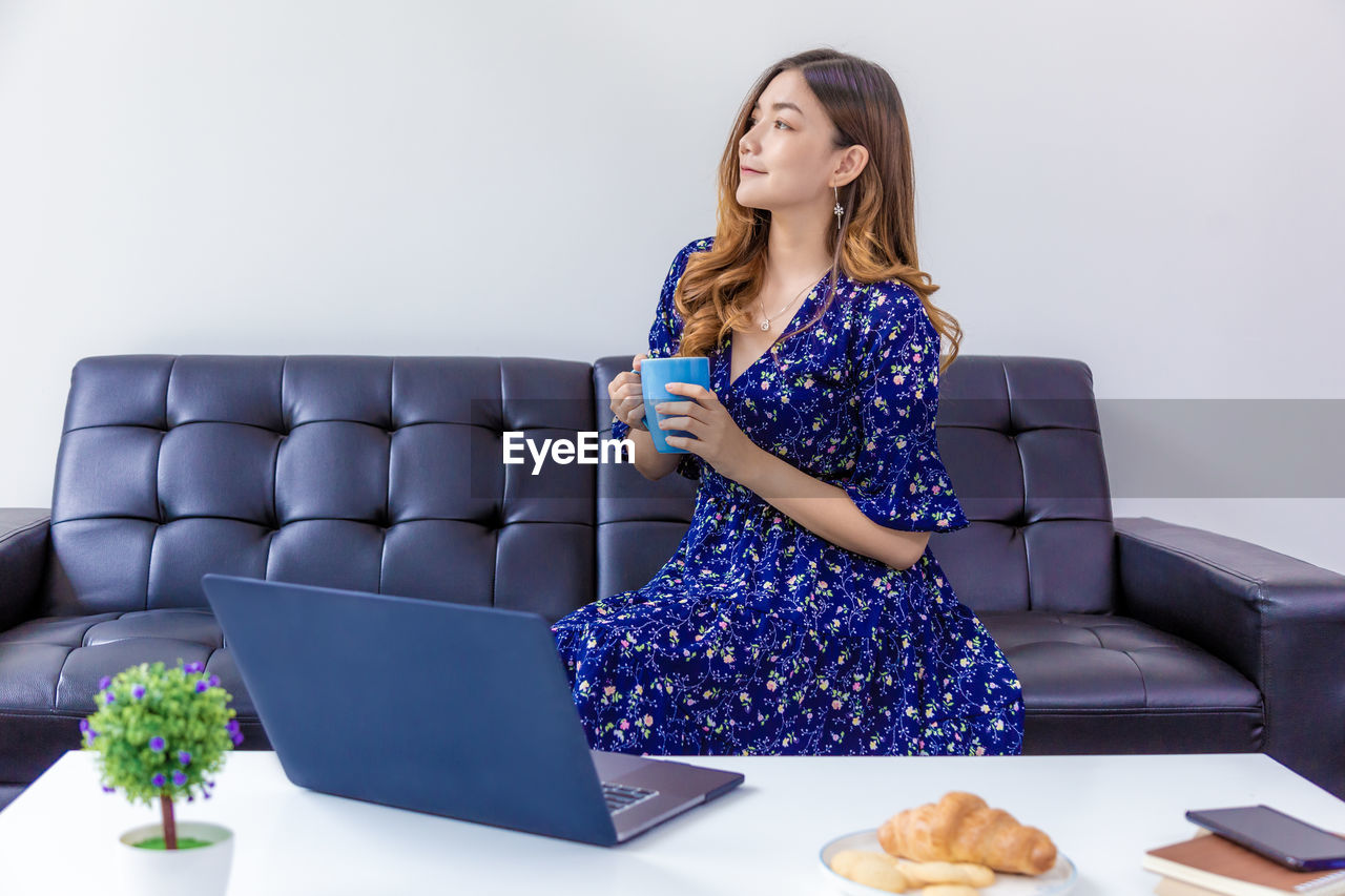 FULL LENGTH OF WOMAN SITTING ON SOFA