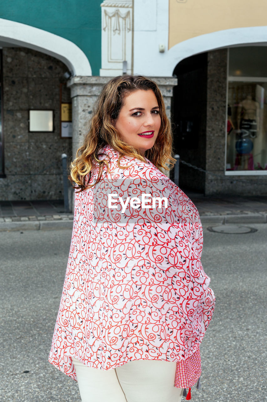 Smiling young blonde oversized woman in fashionable outfit on the street.