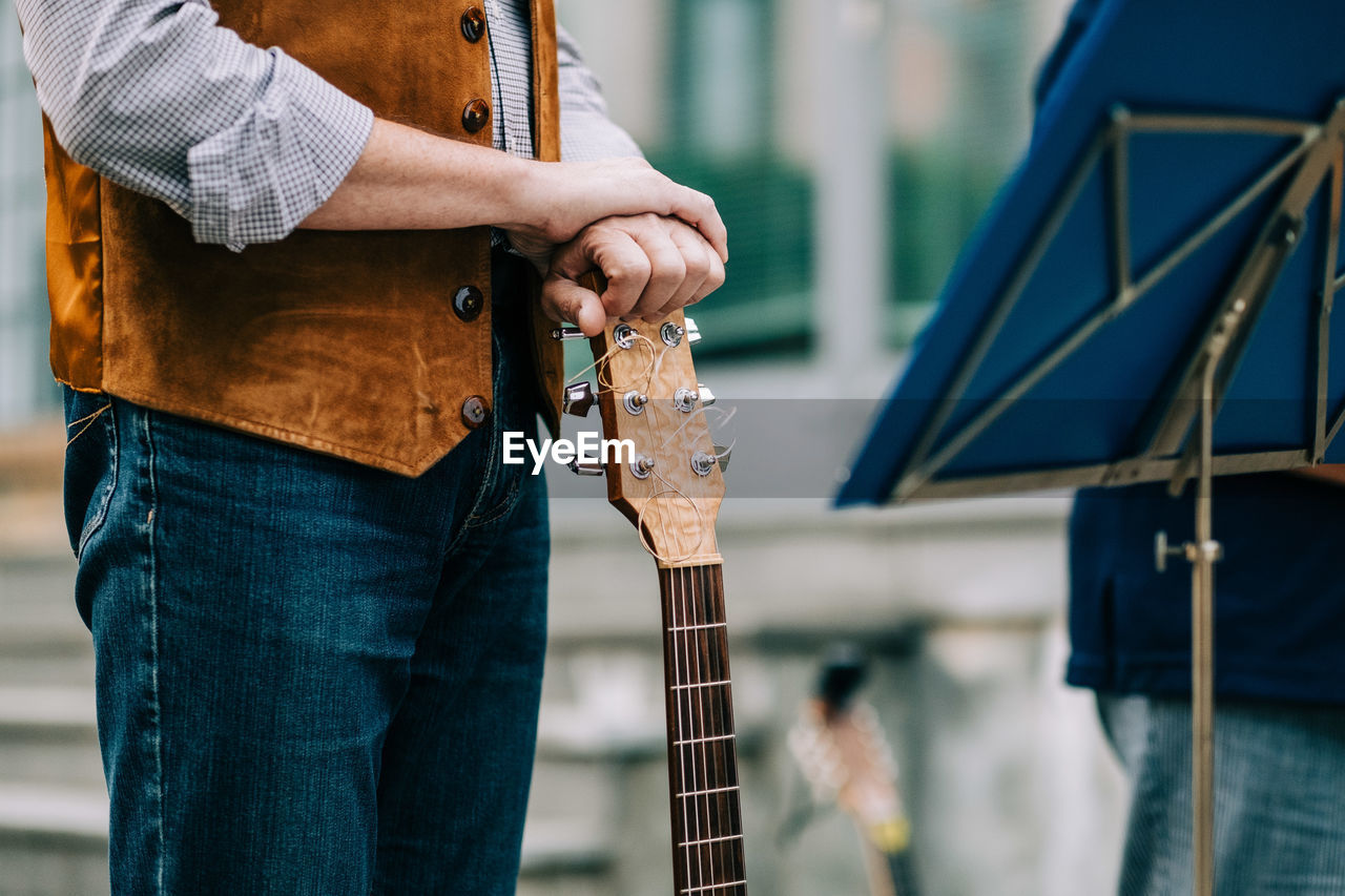 Midsection of man standing with guitar on stage