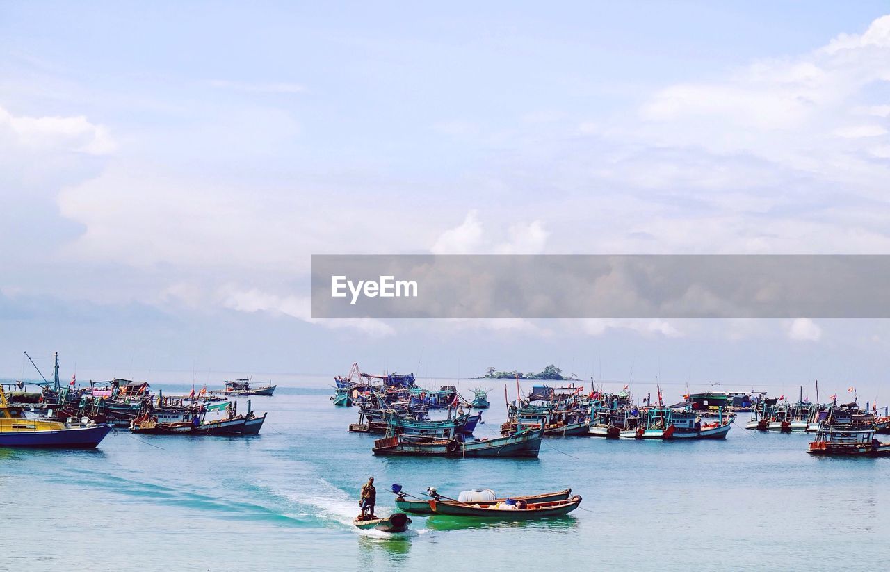 Boats in sea against cloudy sky