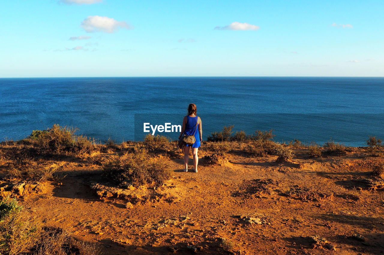 Rear view full length of woman standing on cliff against sea