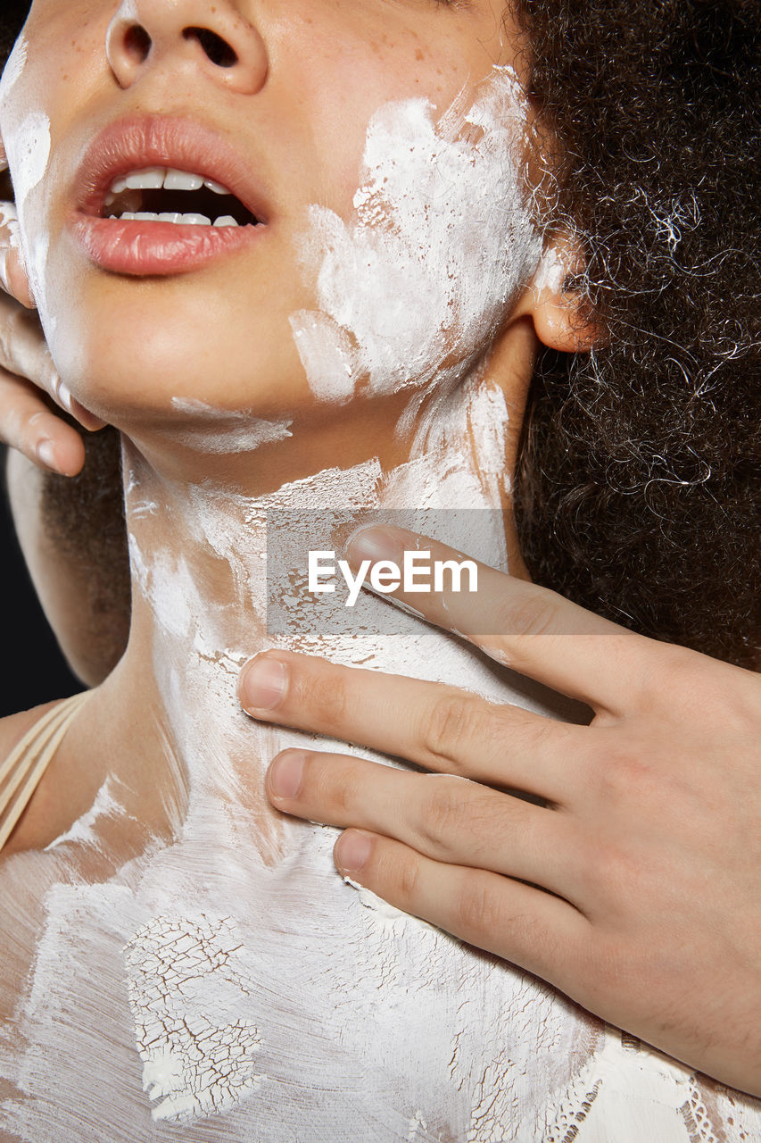 Cropped hand of man applying paint on woman against black background