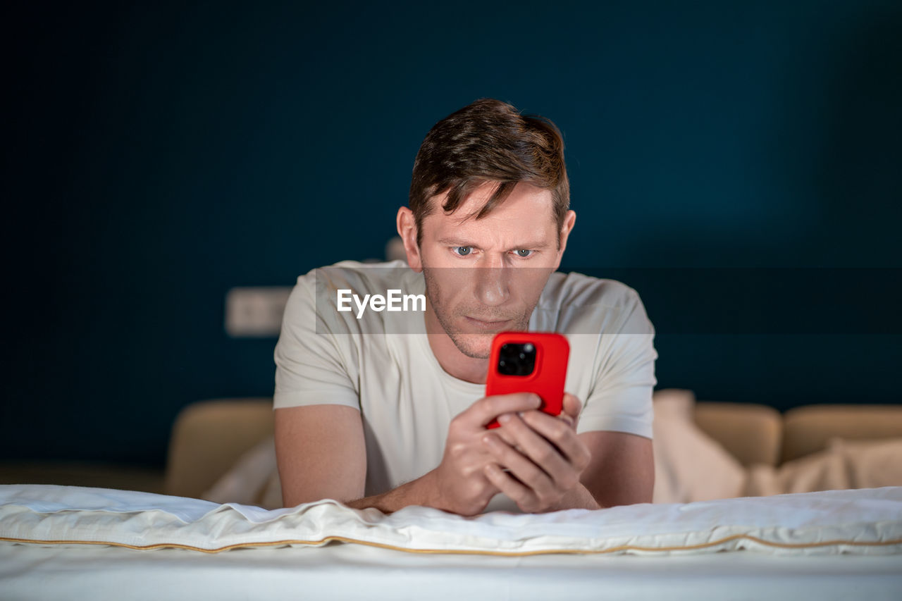 Man uses smartphone lying on bed. online internet purchases solving business problems conducts chat