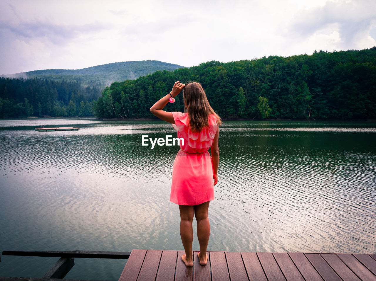 Rear view of young woman standing by lake against sky