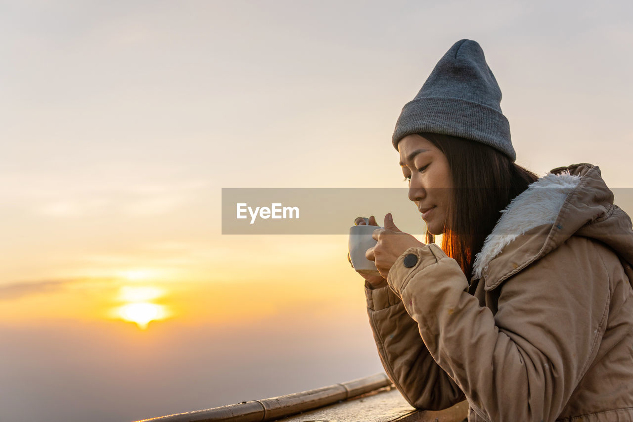 WOMAN WITH ARMS OUTSTRETCHED AGAINST SKY DURING SUNSET