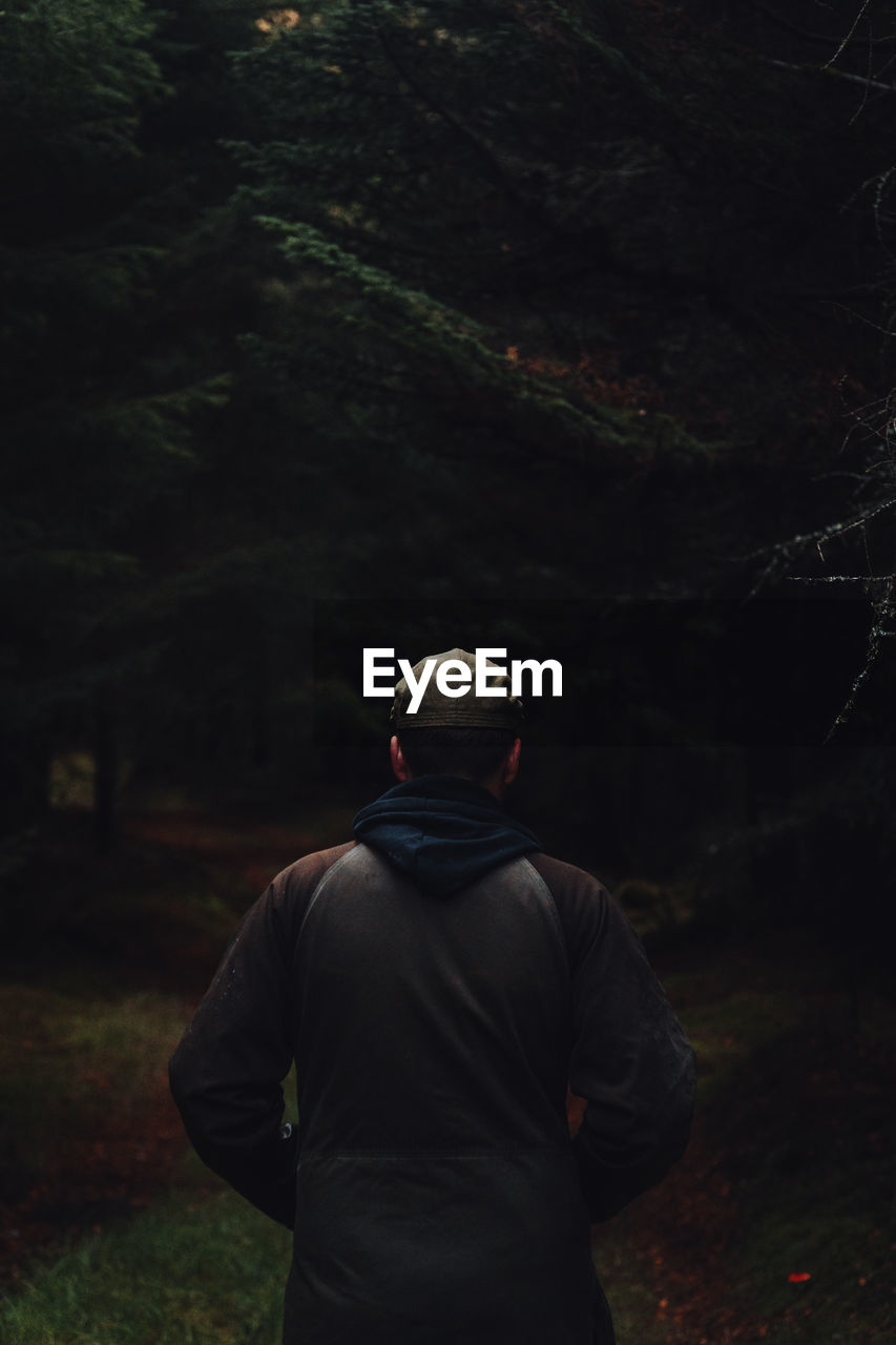 Rear photo of male walking through dark forest.