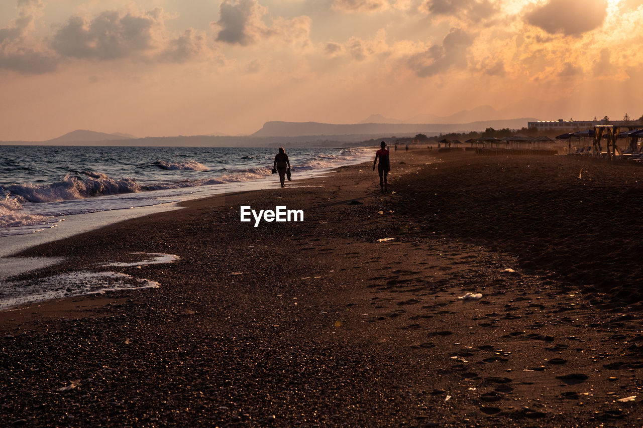 People on beach against sky during sunset