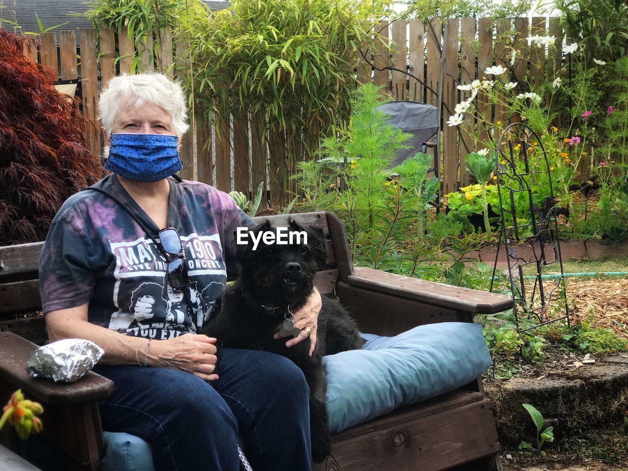 Woman wearing mask sitting with dog at bench