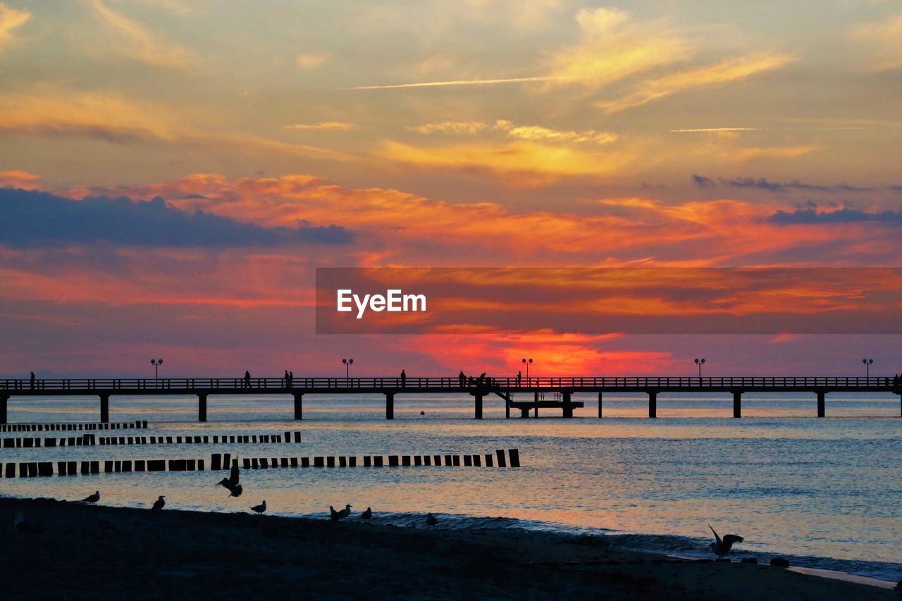 Silhouette pier on beach against sky during sunset