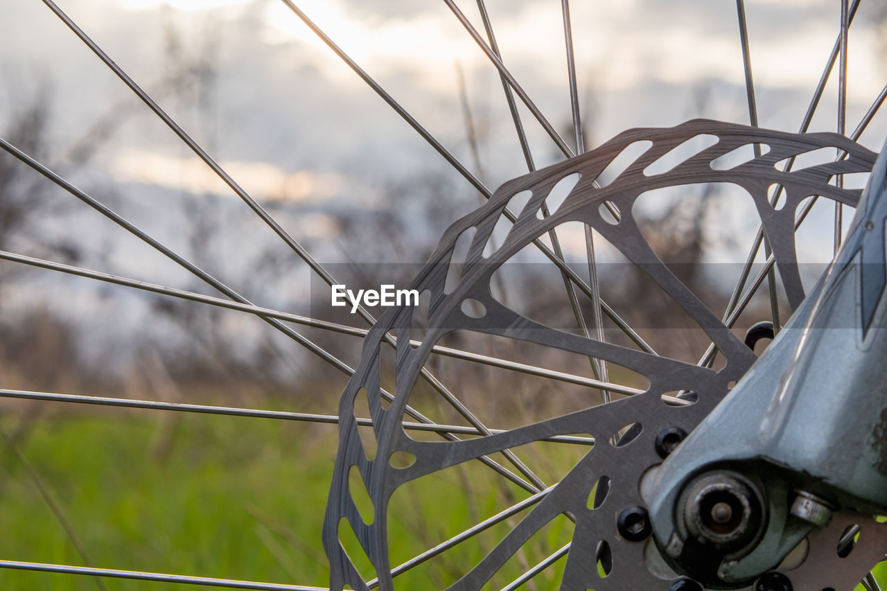 Part of the front disc brake of a mountain bike on a blurry background of grass and sky