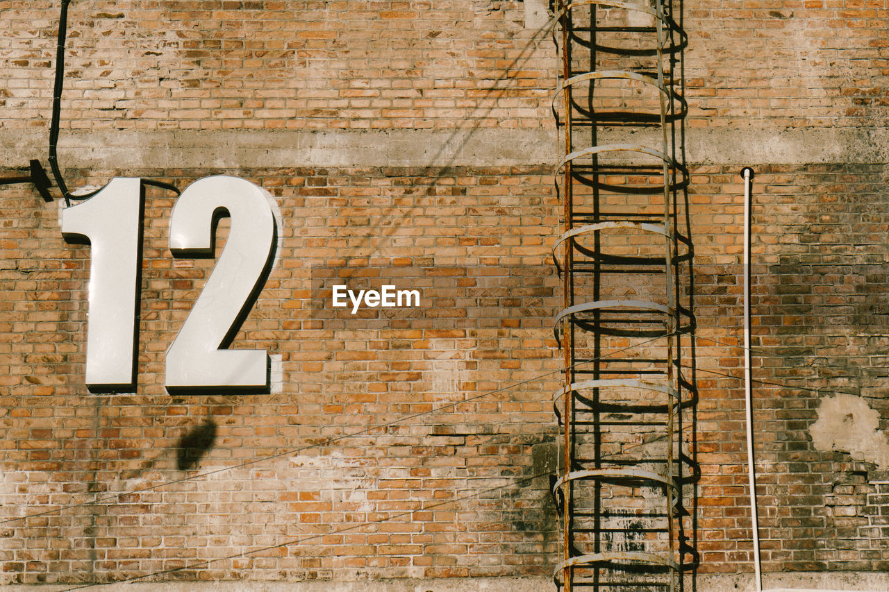 Low angle view of numbers by ladder on brick wall