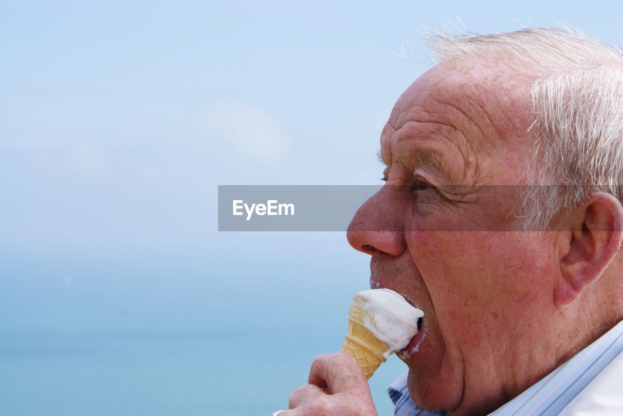 Close-up of senior man eating ice cream against blue sky