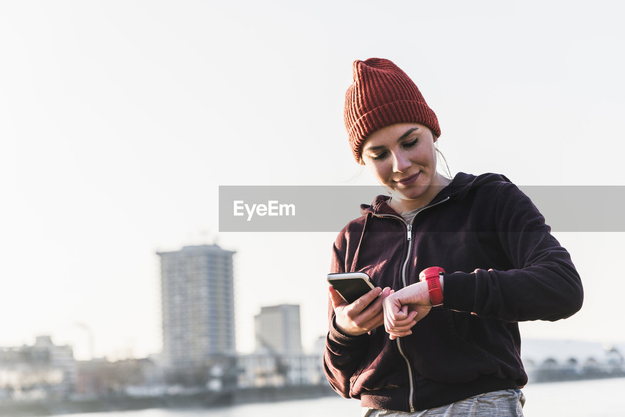 Sportive young woman at the riverside in the city with smartphone and smartwatch