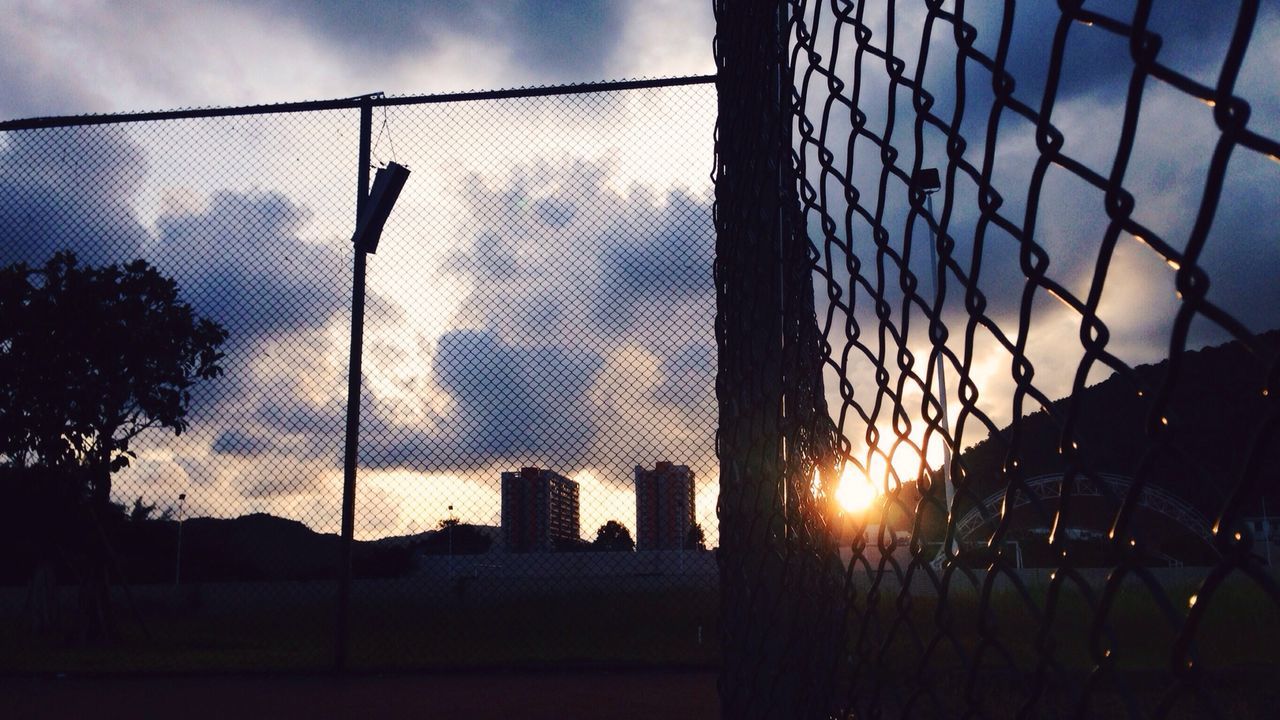 Silhouette chainlink fence against cloudy sky during sunset