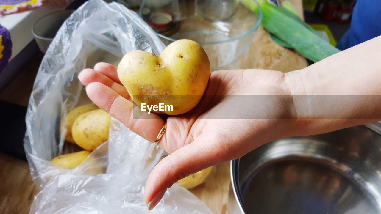 Close-up of cropped hand holding heart shape raw potato in kitchen