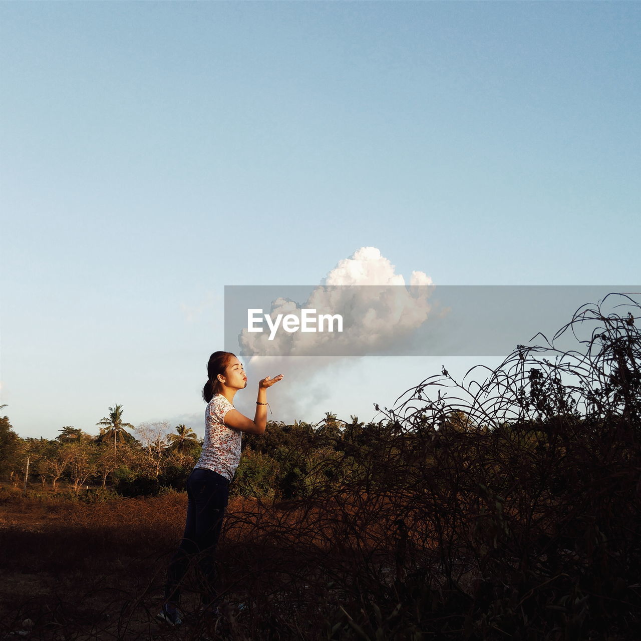 Optical illusion of woman blowing smoke while standing against sky