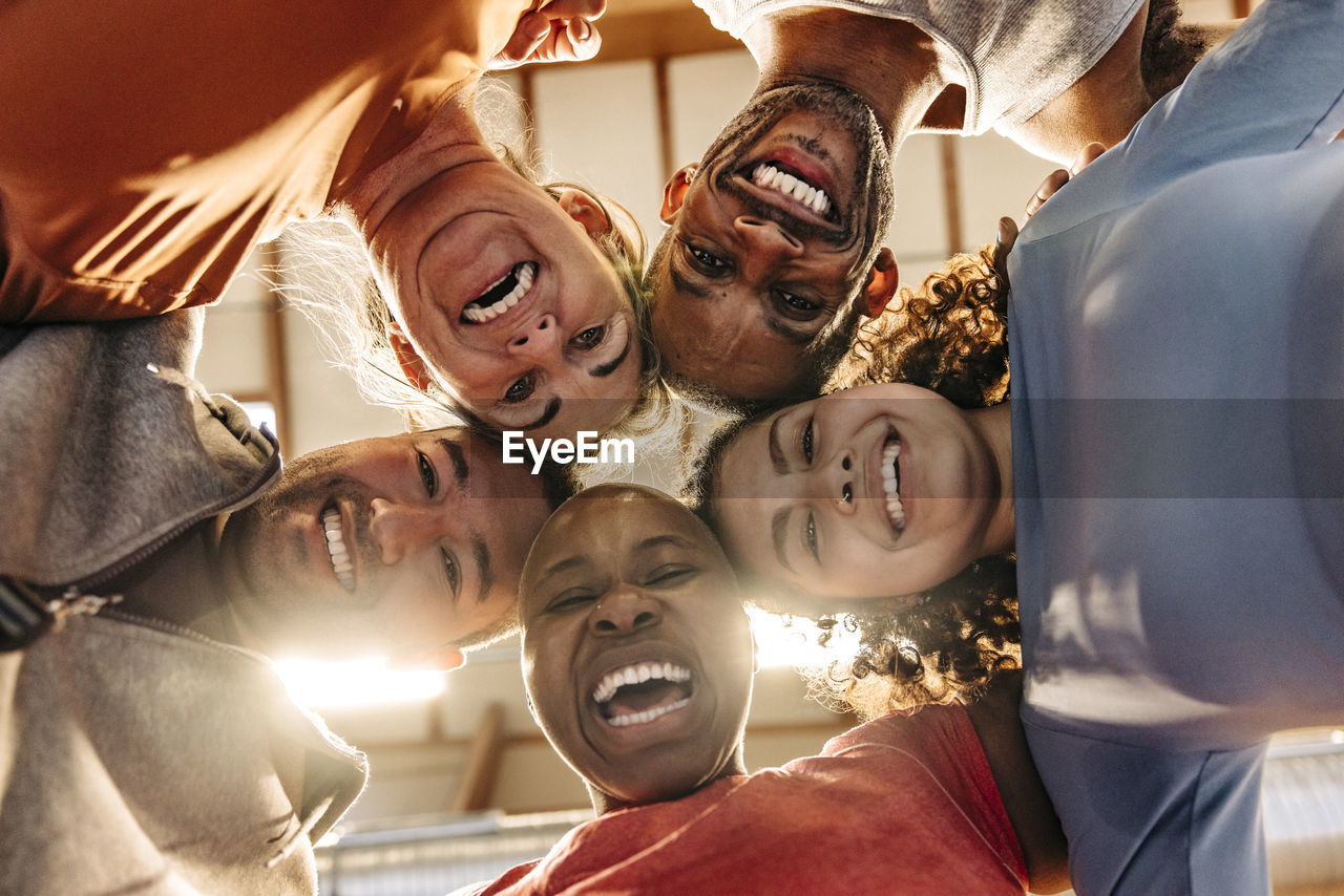 Happy male and female athletes laughing while huddling together at sports court