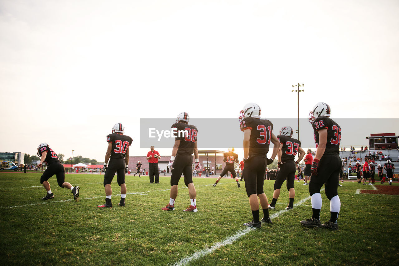 American football team playing on grassy field against sky